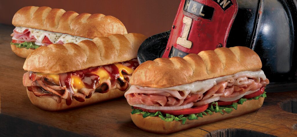 image of 3 different sub sandwiches and a firefighter's helmet