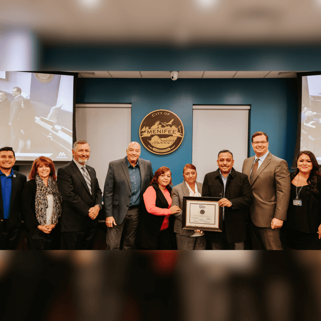 A group of people standing in front of the Menifee city seal, with one person holding a framed certificate from Anguiano’s Bakery as part of the Business Spotlight program.
