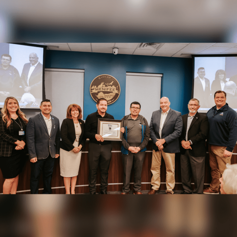 A group of people stands together in a room with a podium and the City of Menifee seal on the wall. One person in the center holds a framed certificate recognizing Black Bear Diner as Menifee's Business Spotlight for March.