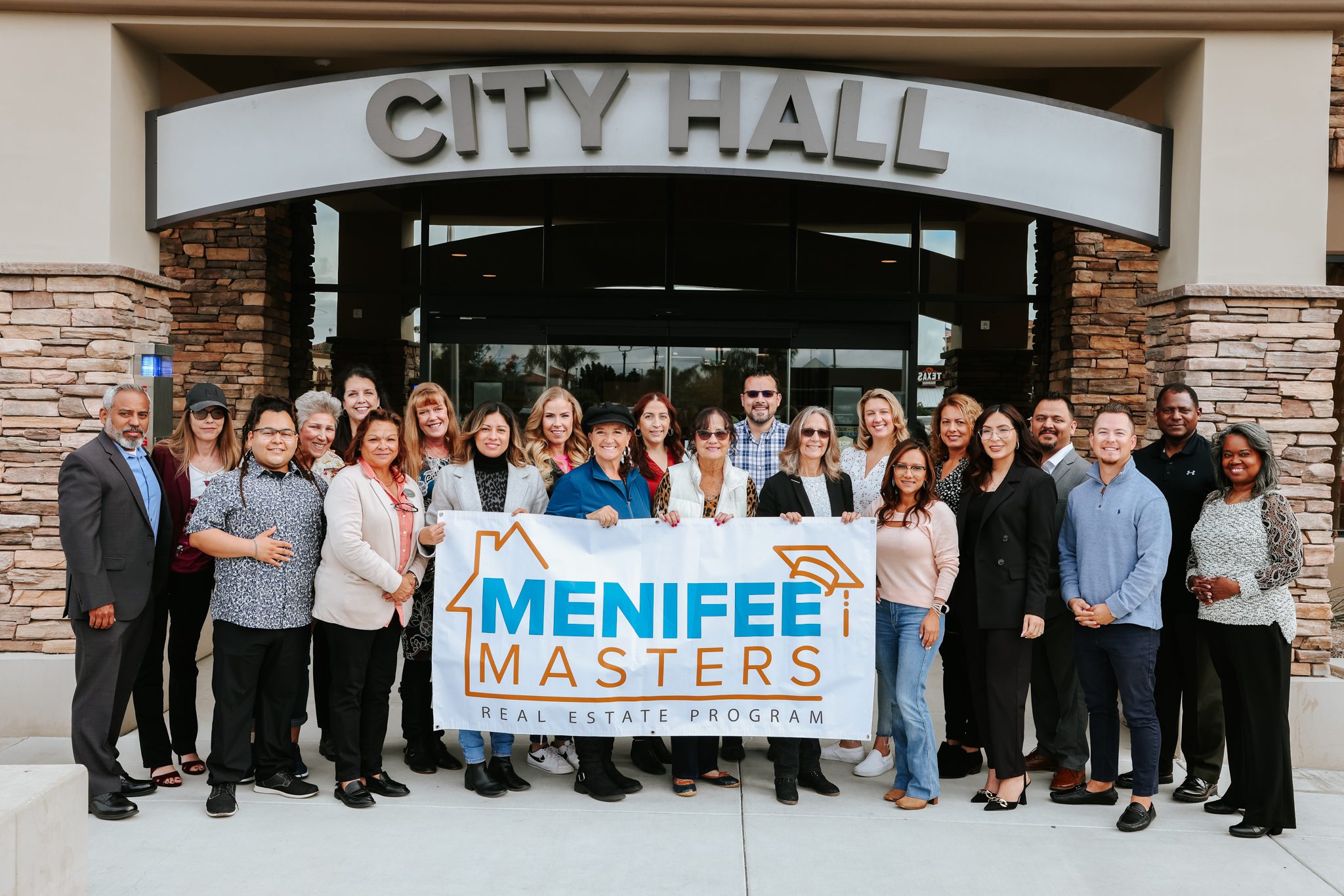 Group of people standing in front of a building labeled "City Hall," holding a banner that reads "Menifee Masters Real Estate Program," showcasing their commitment to the Menifee community.